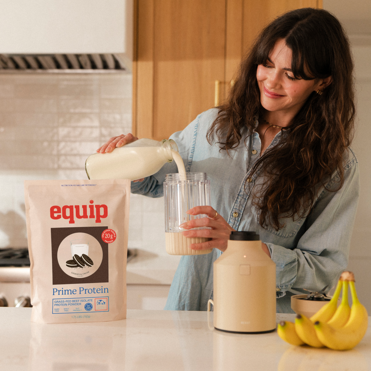 A woman pours milk into a shaker next to a bag of Equip Prime Protein